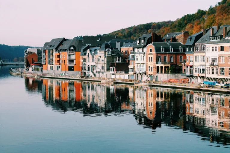 A colorful town reflected in a calm river, nestled between hills.
