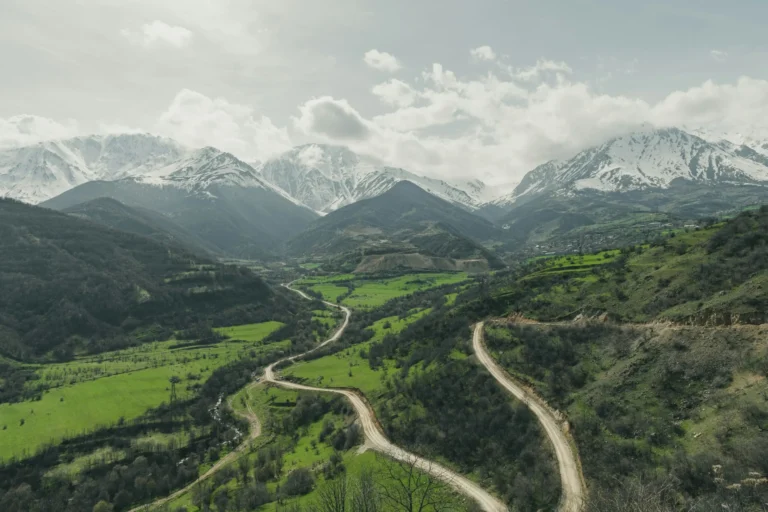 An aerial view of a winding road through a lush green valley surrounded by majestic mountains.