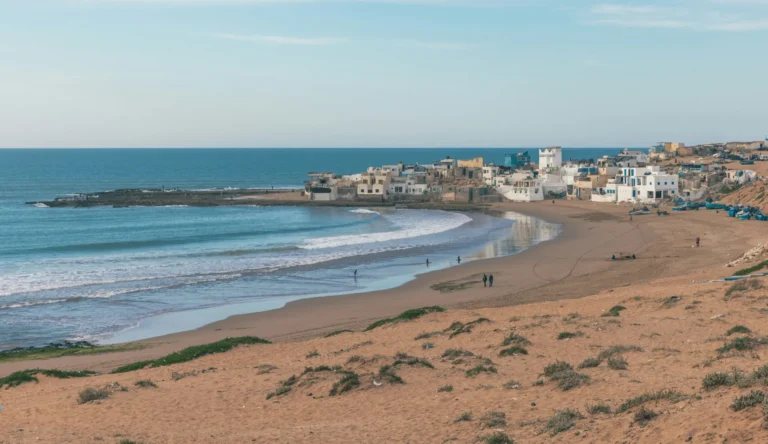 A coastal town with white buildings and a sandy beach next to the blue sea.