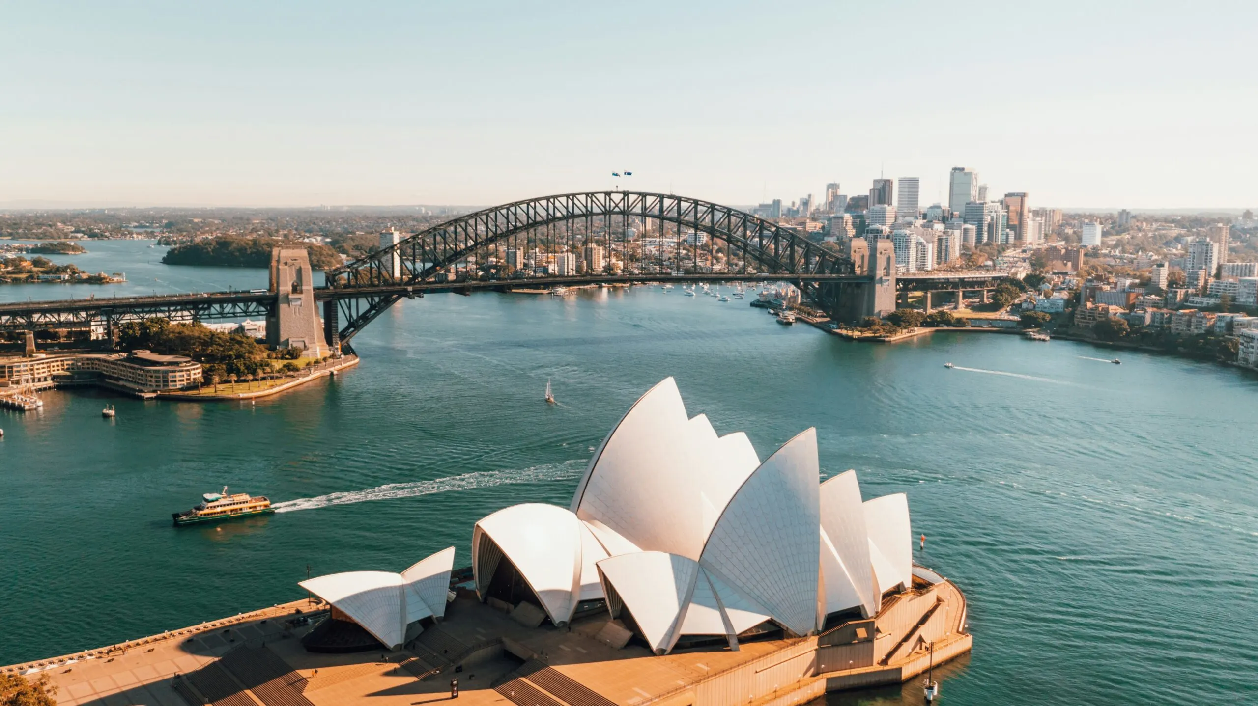 An aerial view of Sydney Harbour, featuring the Opera House and Harbour Bridge, with the city skyline in the background.