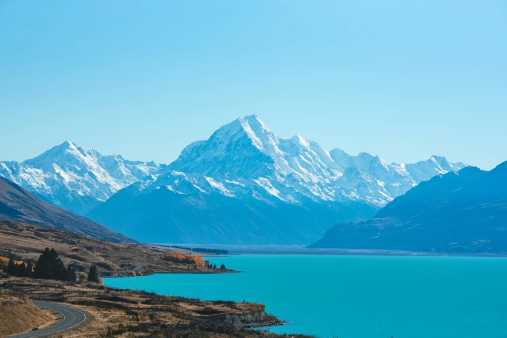 A vibrant turquoise lake in the foreground with a towering, snow-capped mountain range in the background.