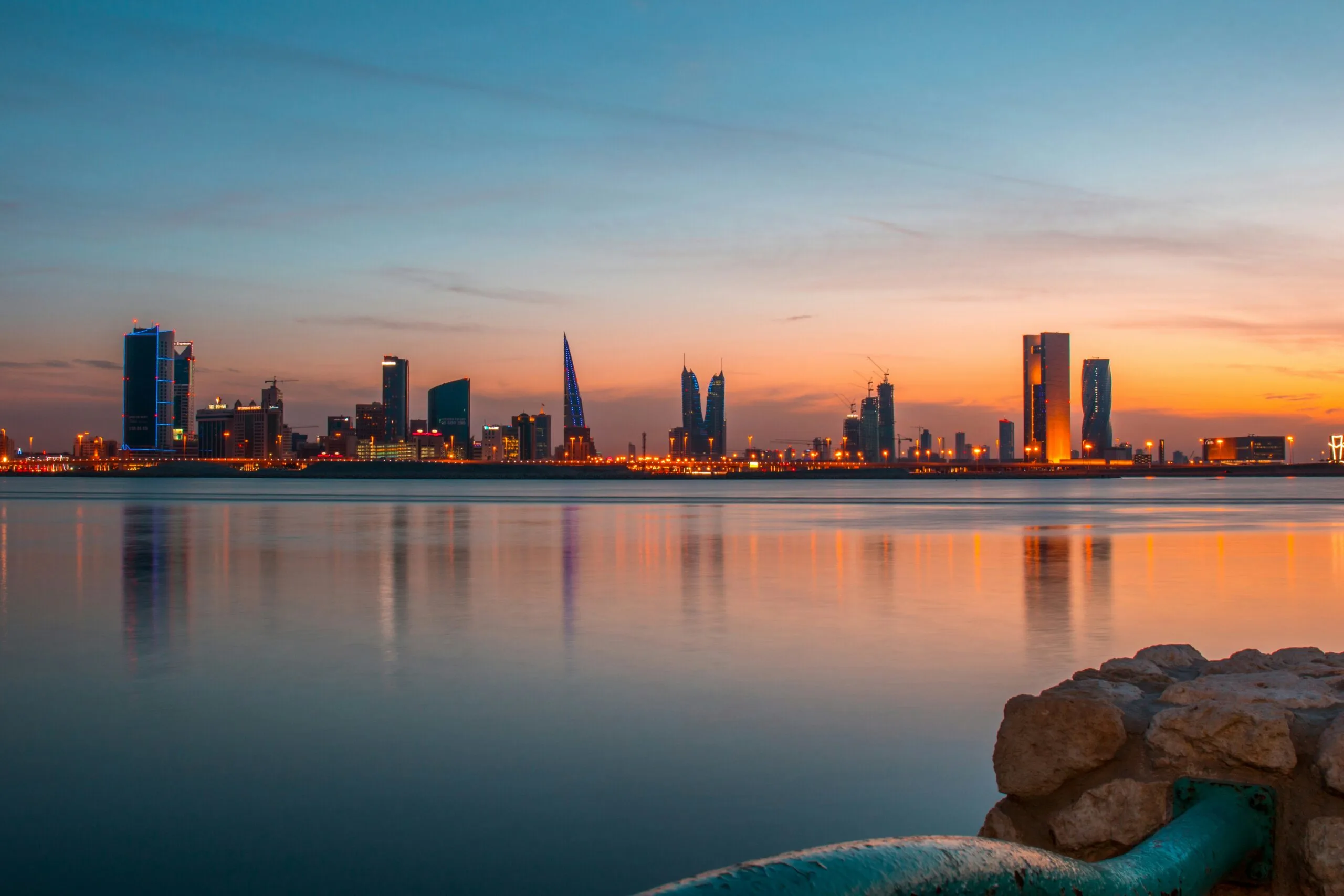 A city skyline across a body of water at sunset, with buildings silhouetted against a colorful sky.