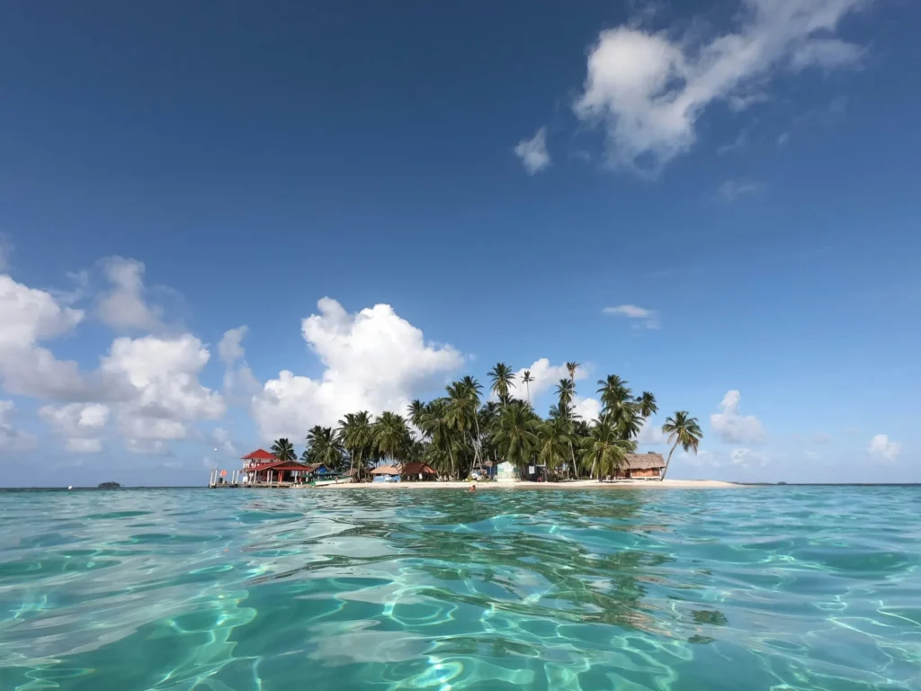 A small, tropical island with palm trees, surrounded by clear turquoise water.