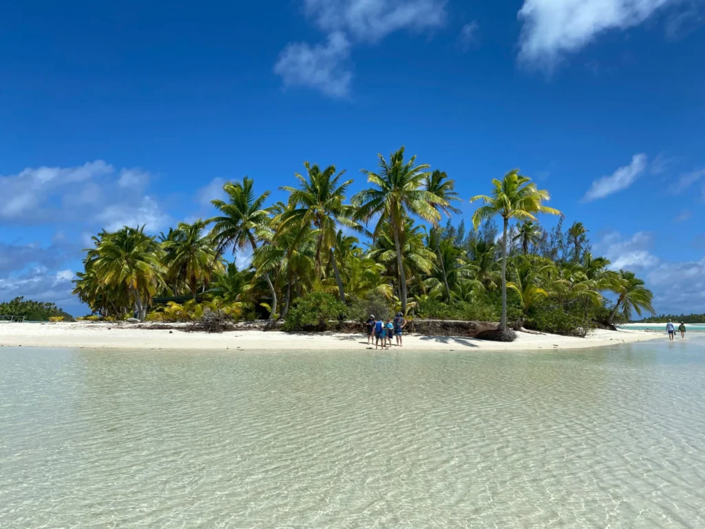 A small tropical island with palm trees and a white sandy beach in clear turquoise water under a blue sky.