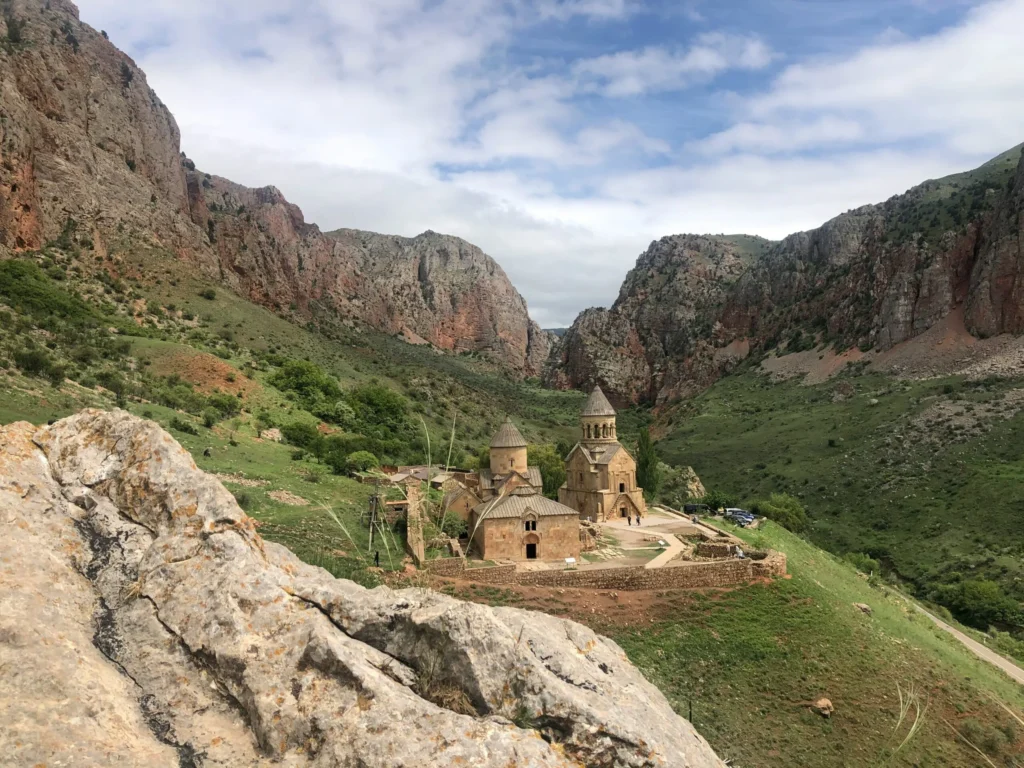 Ancient rock-cut dwellings or structures are nestled into a rugged mountain landscape with a winding path below.