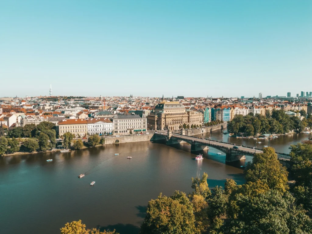 A map of Europe with Sweden highlighted in green. A lone figure walking across a vast, snow-covered landscape with sparse trees. A map of Europe with Austria highlighted in green. An evening cityscape of Prague with Charles Bridge and Prague Castle illuminated. A panoramic view of a city along a river with bridges and historical buildings.