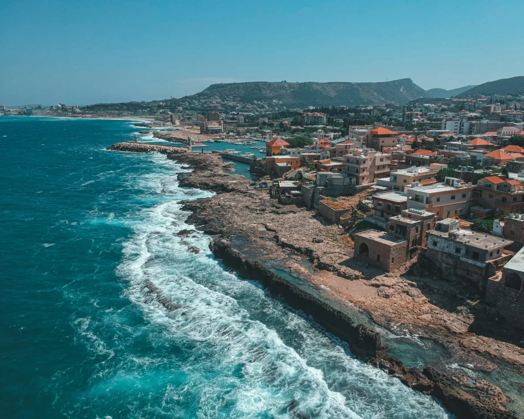 An aerial view of a rugged coastline with waves crashing against rocks and a town stretching along the shore.