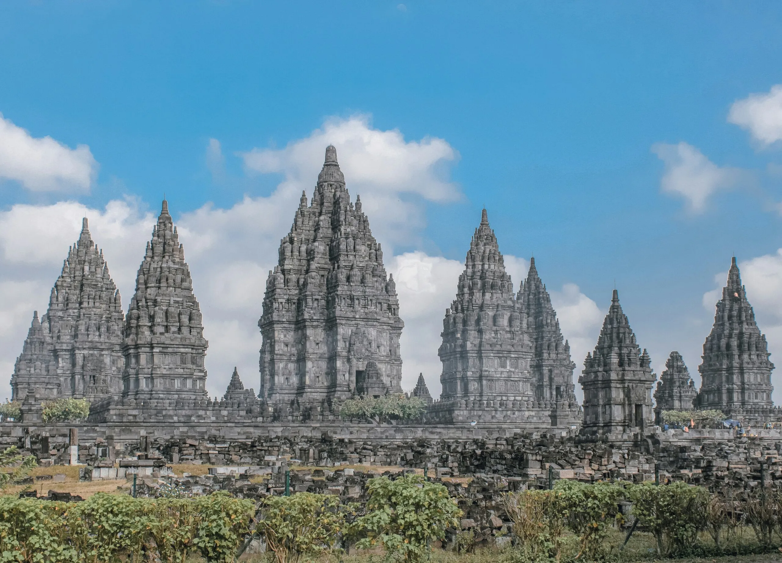 The ancient Hindu temple complex of Prambanan, with its towering, intricately carved structures under a blue sky.