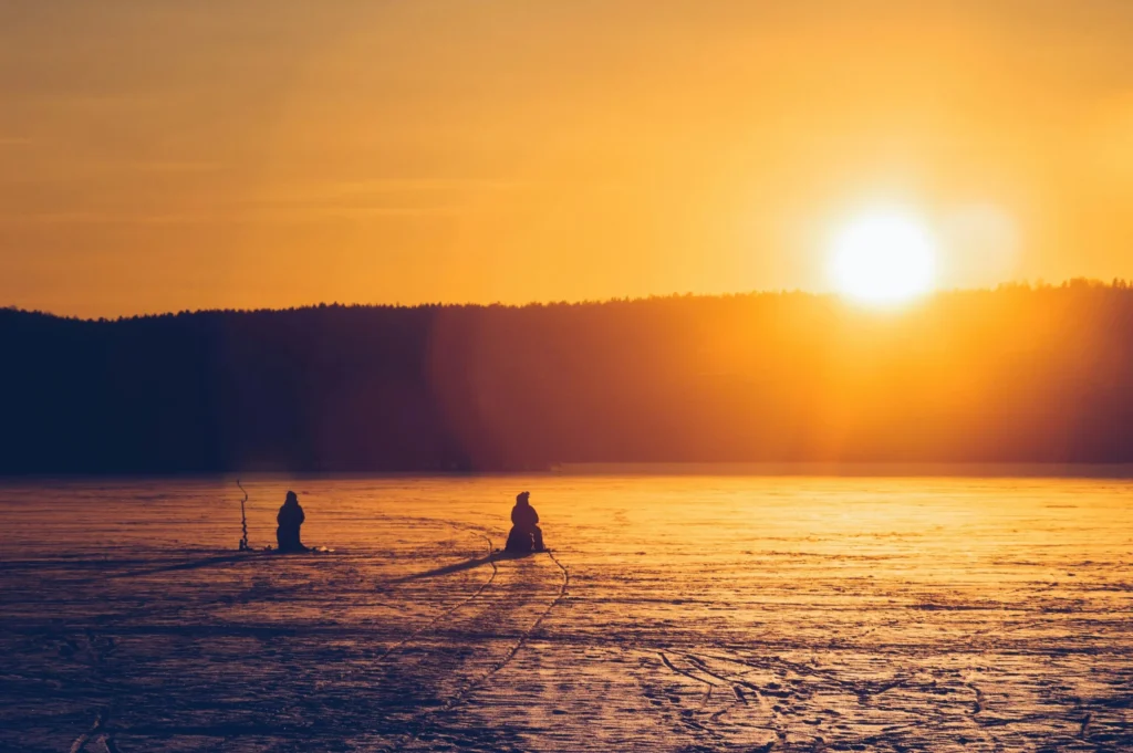 Two figures on a vast, flat expanse of ice or sand, under a dramatic sunset sky.