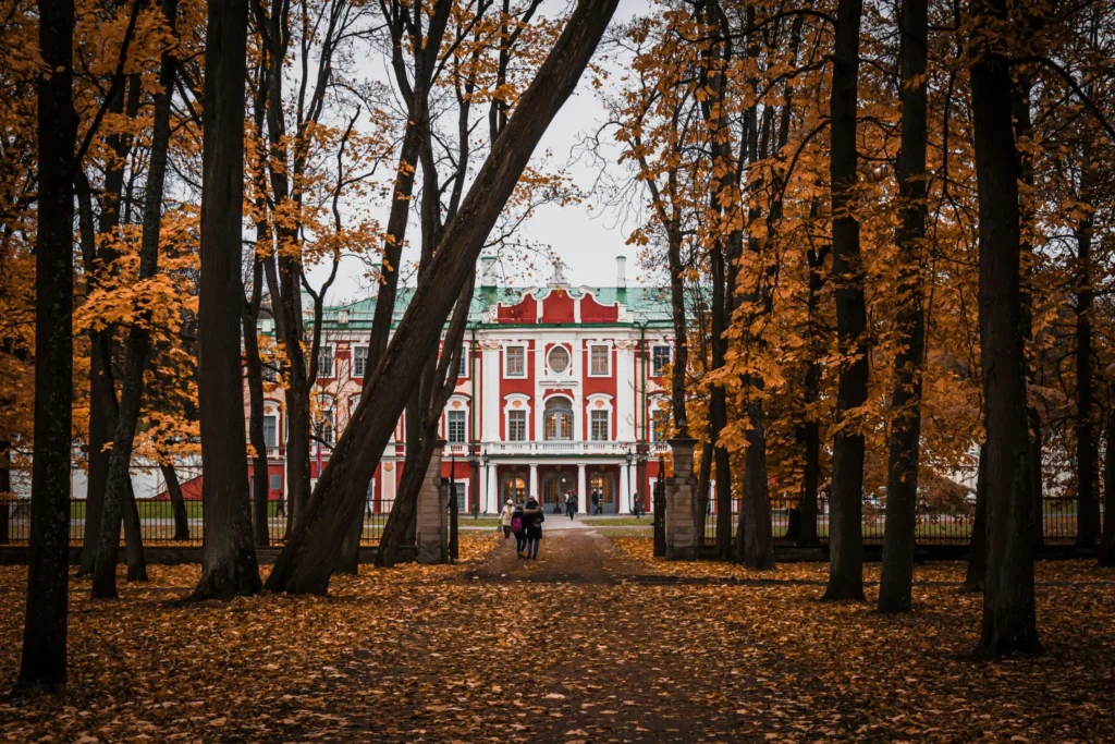 A large, grand white building with a red roof, nestled among tall, bare trees in an autumn setting.