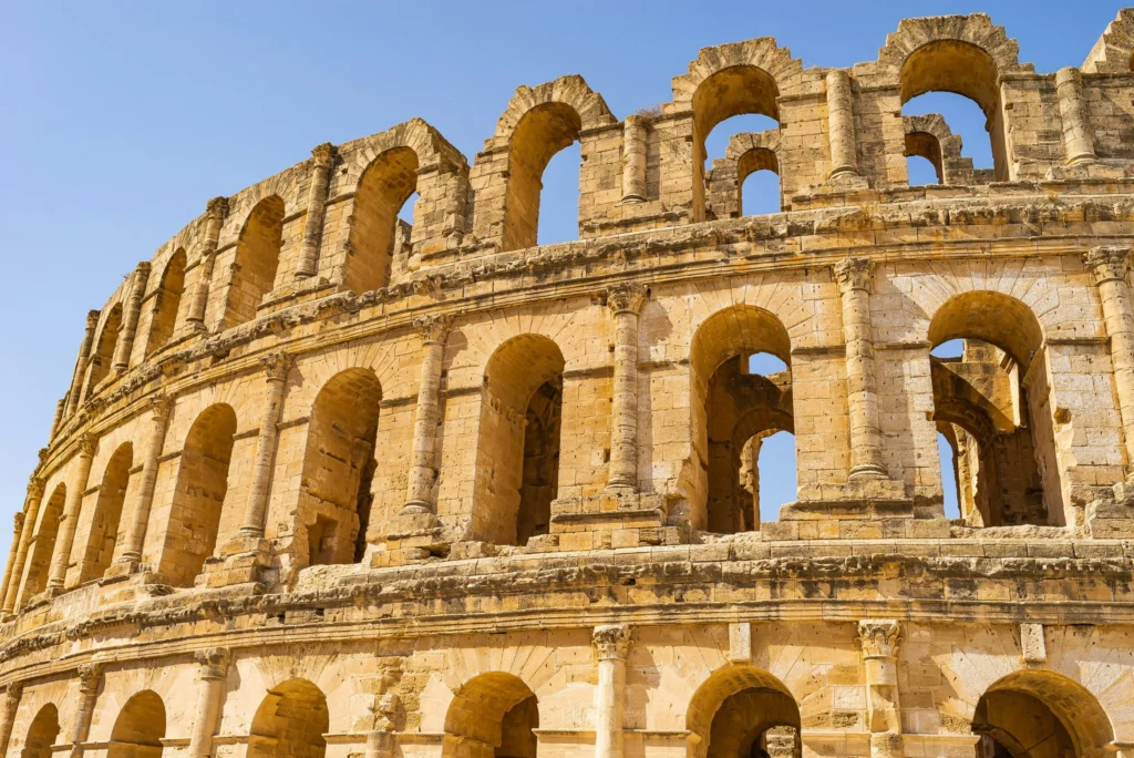 The ancient Roman amphitheater of El Jem, with its impressive arches, under a clear sky.