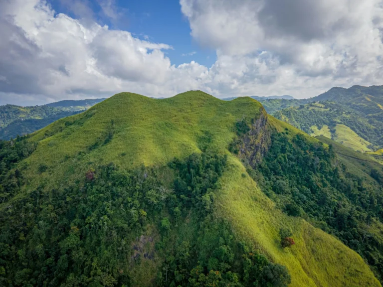 An aerial view of lush green mountains under a partly cloudy sky.
