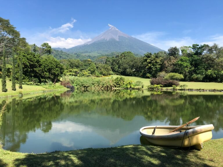 A serene lake with a small boat, reflecting a volcano and lush green surroundings.