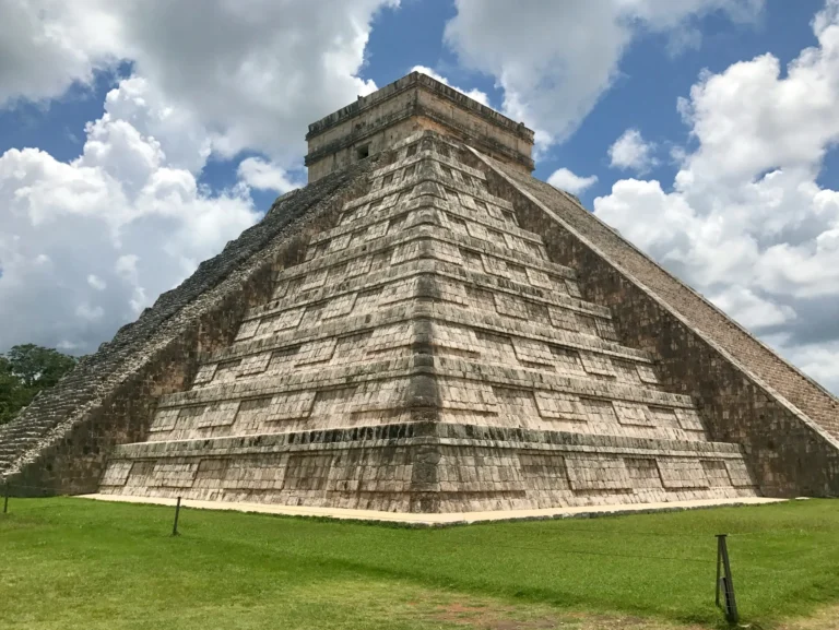 The ancient Mayan pyramid of Chichen Itza under a partly cloudy sky.