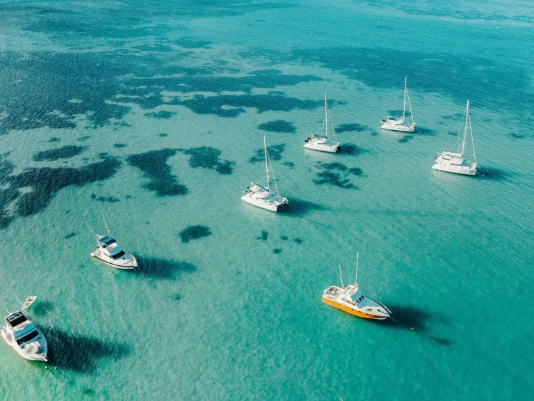 An aerial view of clear turquoise water with several boats anchored.