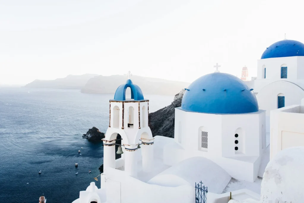 White buildings with blue domes perched on a cliff overlooking the sea in Santorini, Greece.