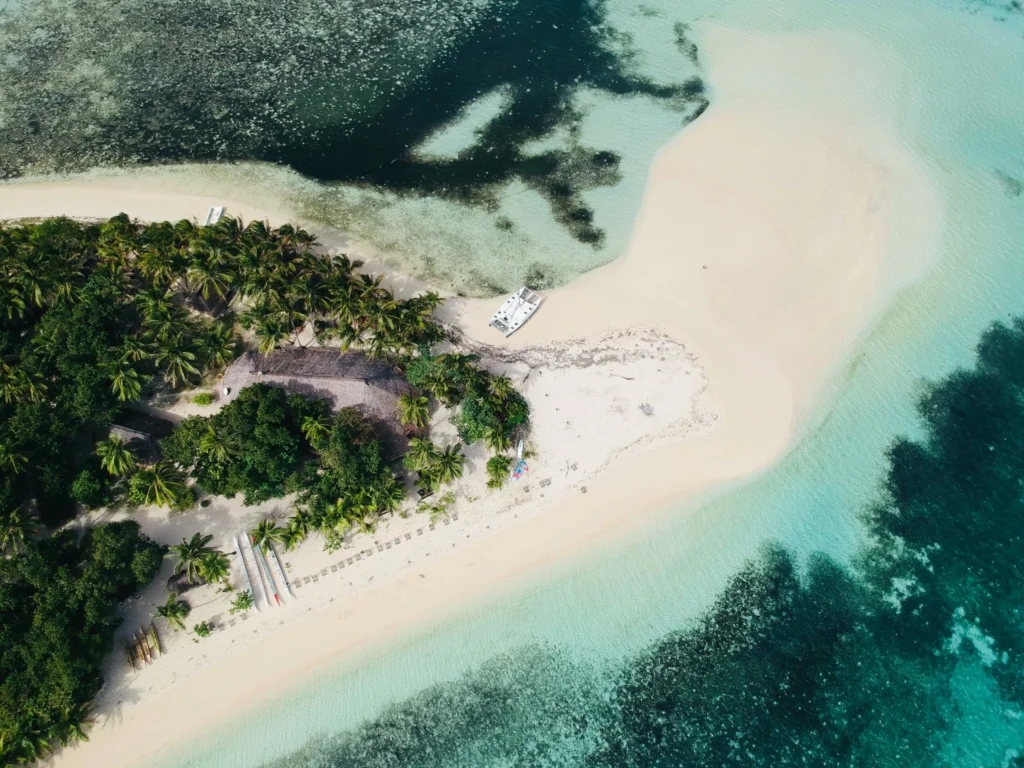 An aerial view of a tropical island with lush green vegetation, white sandbars, and clear turquoise water.