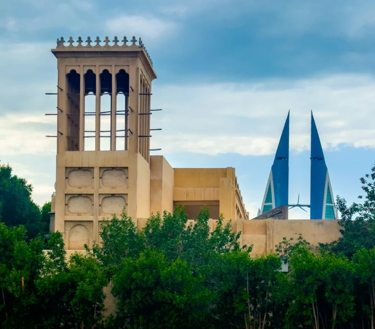 A traditional wind tower building stands alongside modern twin skyscrapers in a city.
