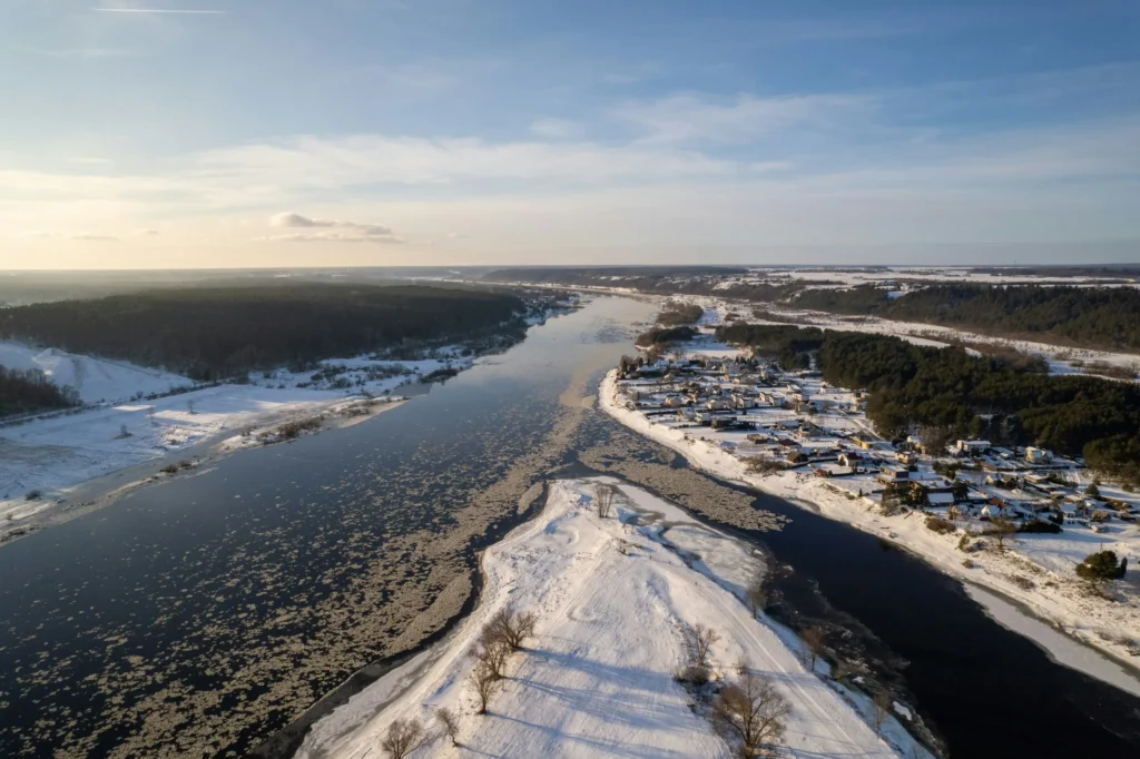 An aerial view of a wide river flowing through a snow-covered landscape.