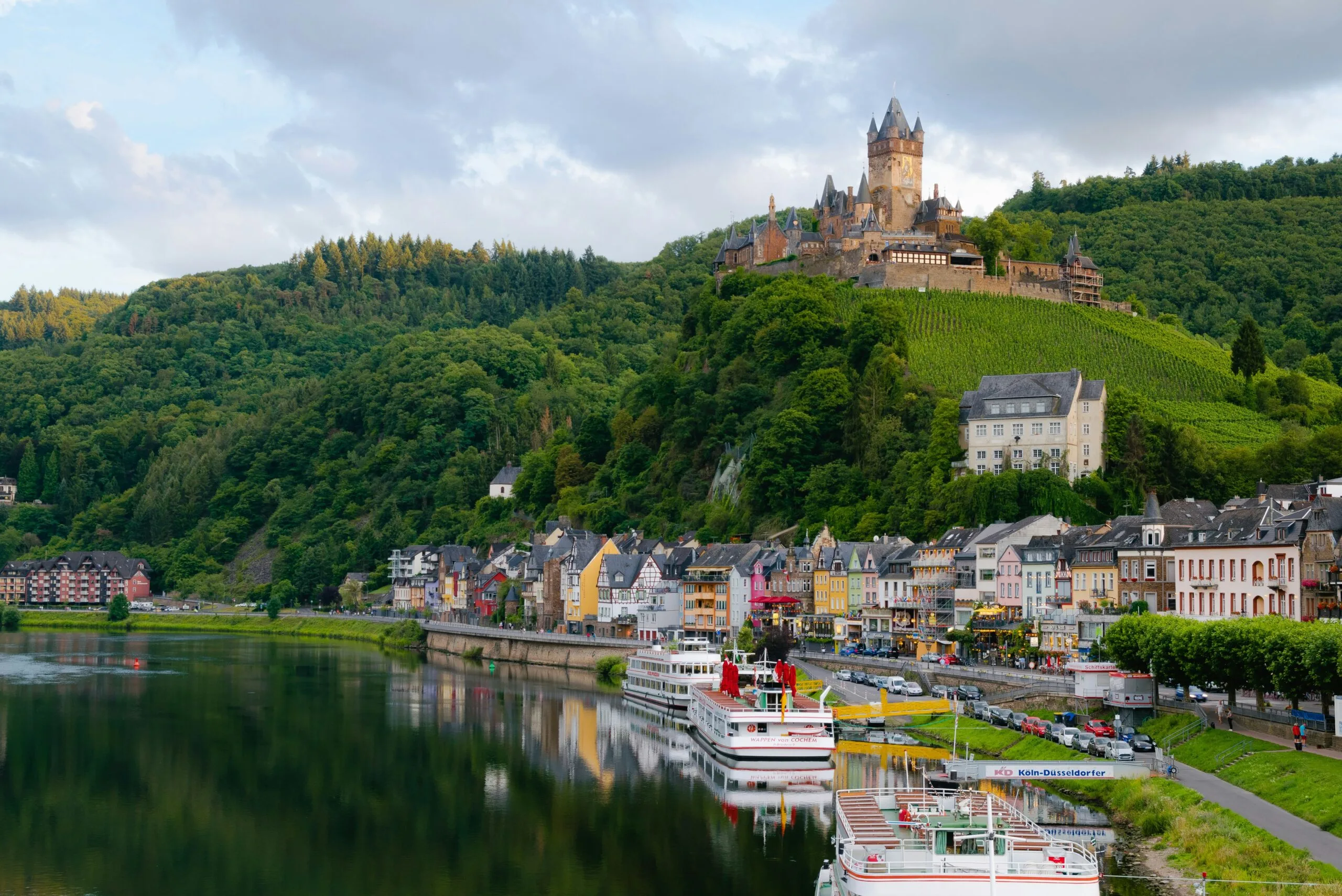 A picturesque town nestled beside a river with a castle perched on a hill above.