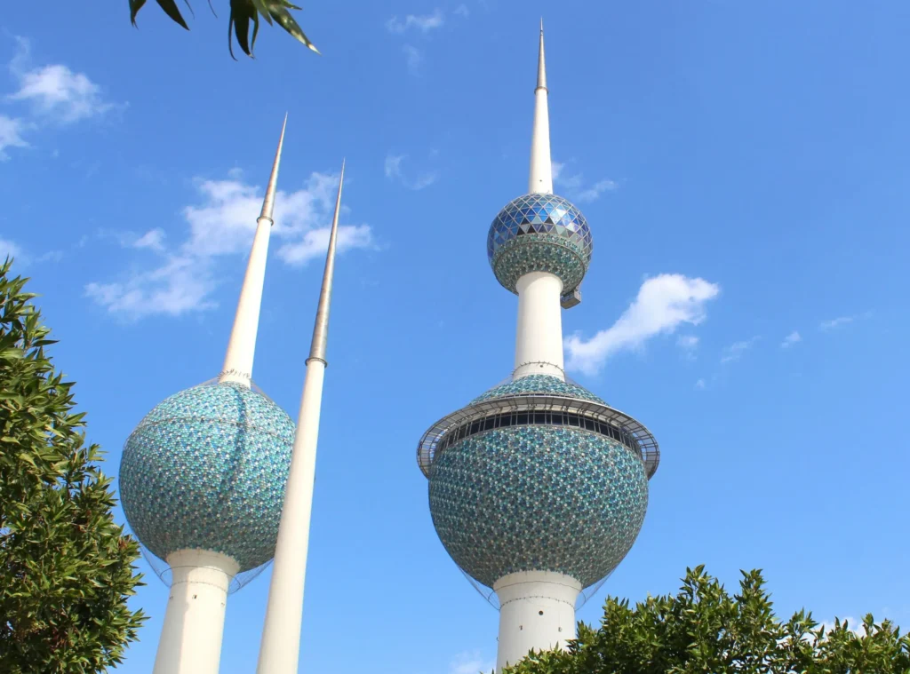 The Kuwait Towers, distinctive tall structures with spheres, against a blue sky with some greenery.