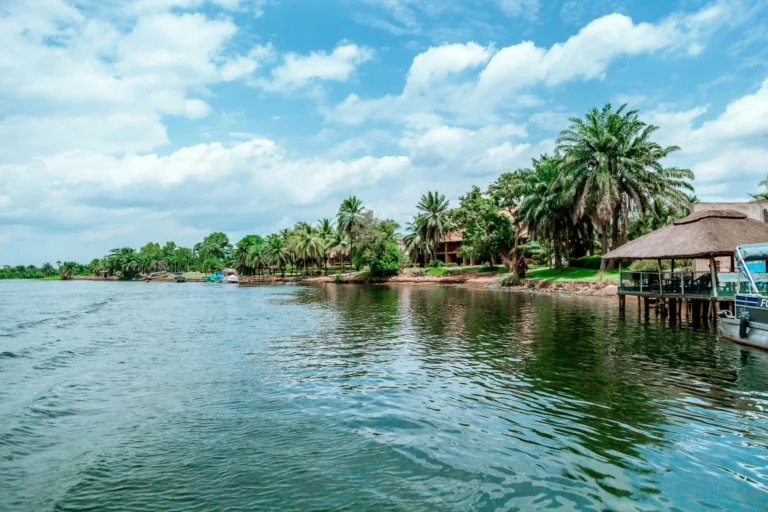 A wide river or lake with lush green banks and buildings under a cloudy sky.