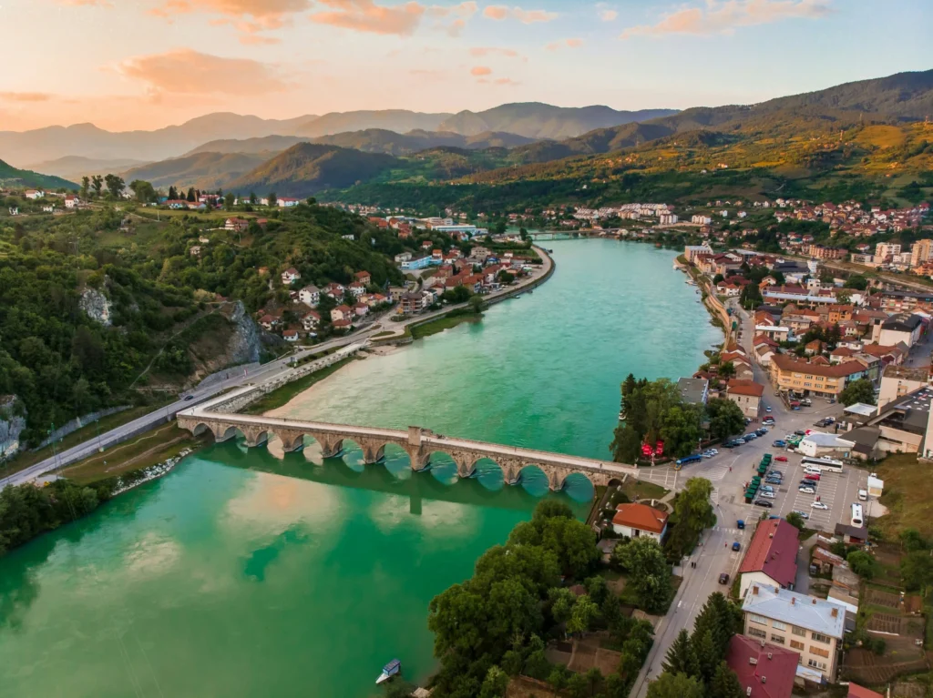 A scenic town with a bridge over a turquoise river, surrounded by hills.