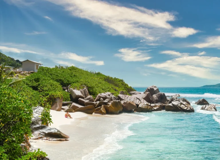 A secluded beach with clear turquoise water, white sand, and large granite boulders.