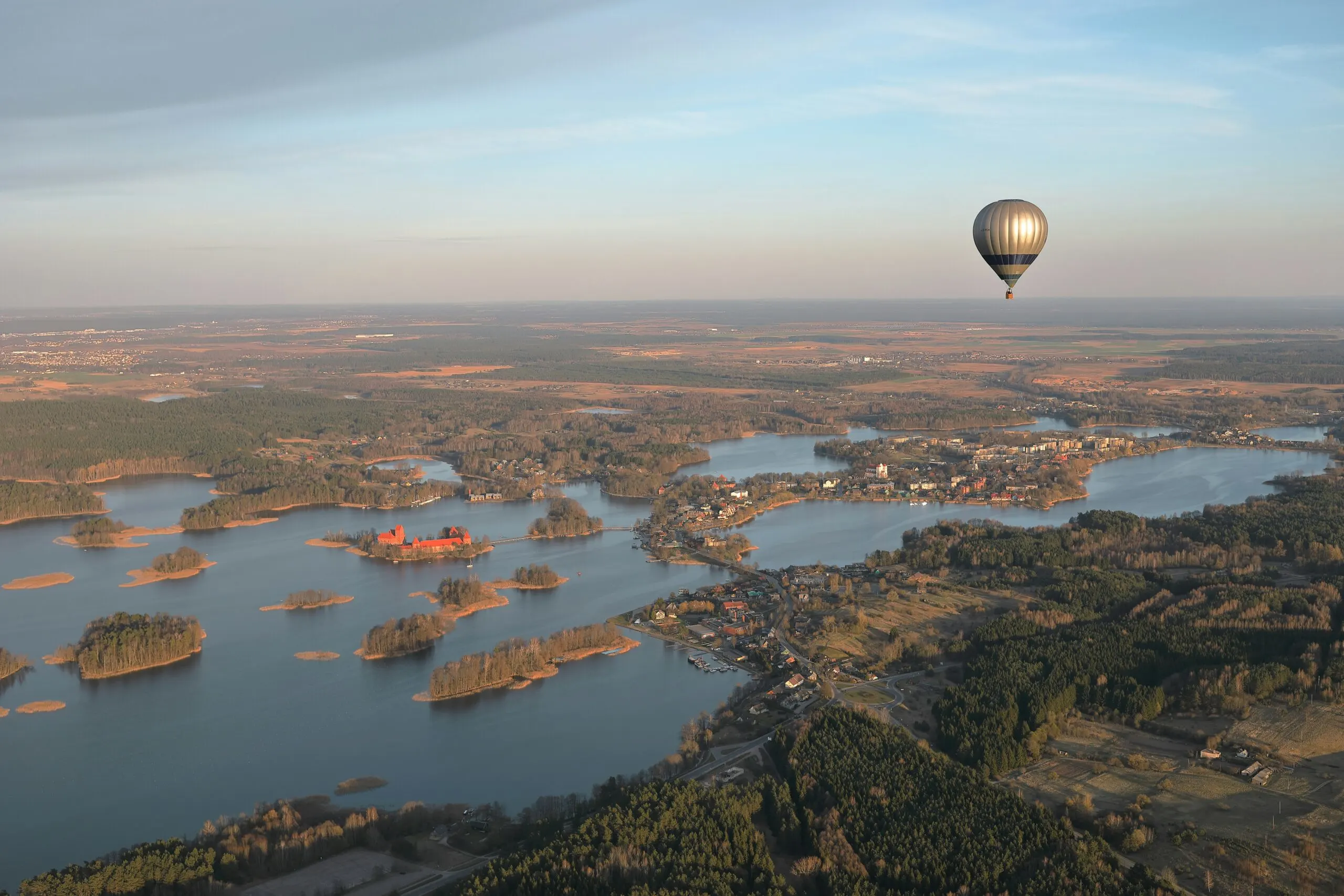 A hot air balloon floats over a landscape with a large body of water and islands during sunrise or sunset.
