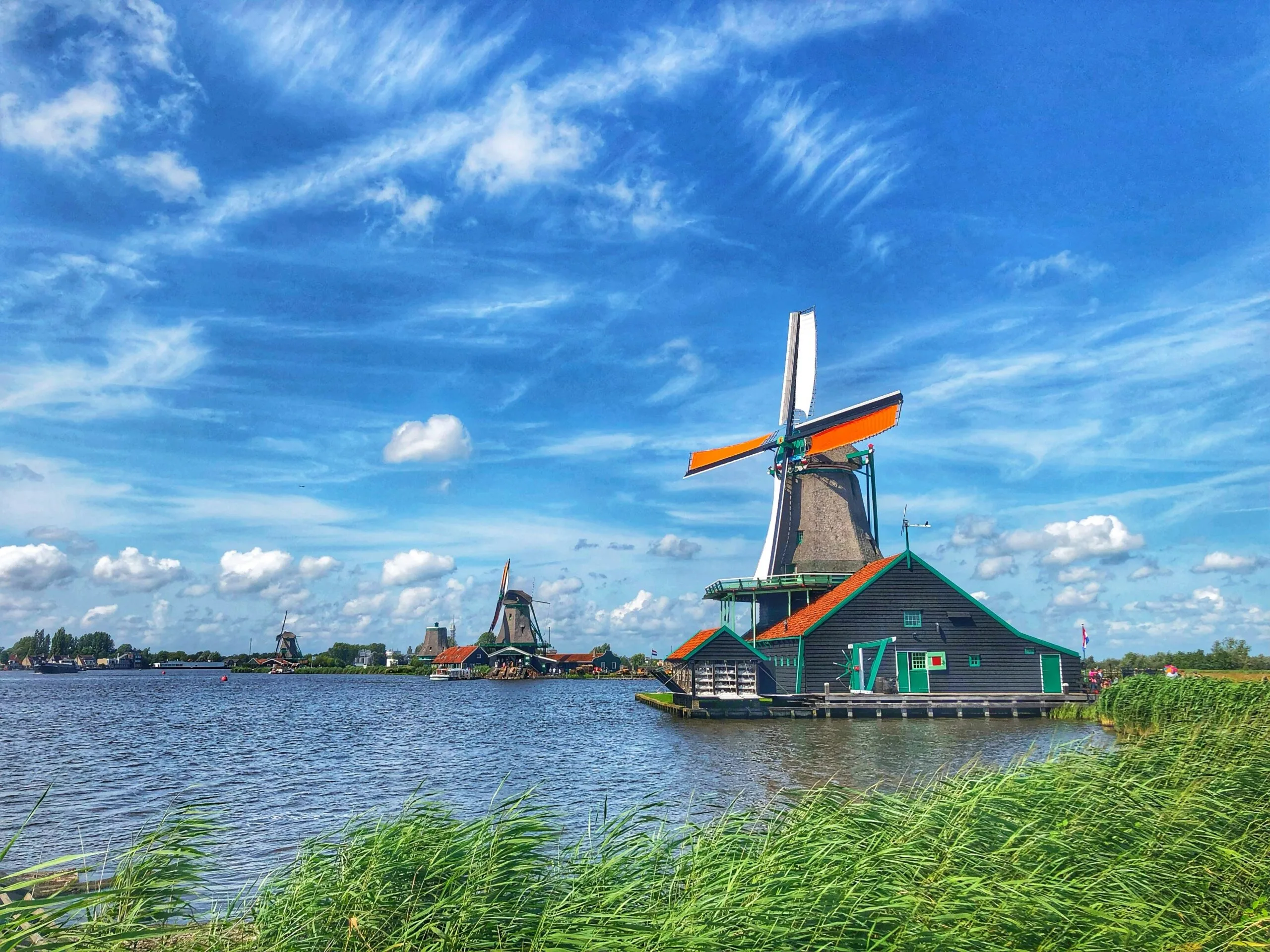 A traditional Dutch windmill by a body of water under a blue sky with clouds.