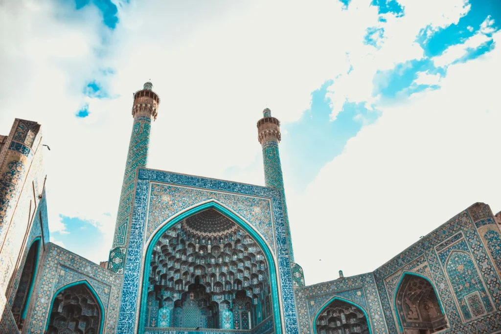 An intricately tiled entrance or facade of a mosque or traditional building, with two minarets reaching towards the sky.