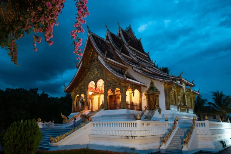 A traditional Lao temple, possibly Wat Xieng Thong, illuminated at dusk with intricate architecture.