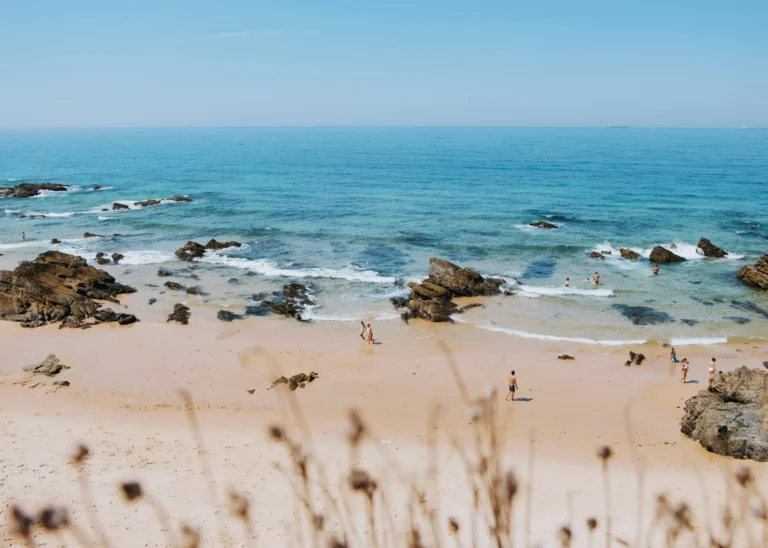 A rocky beach with clear blue water and gentle waves under a bright sky.