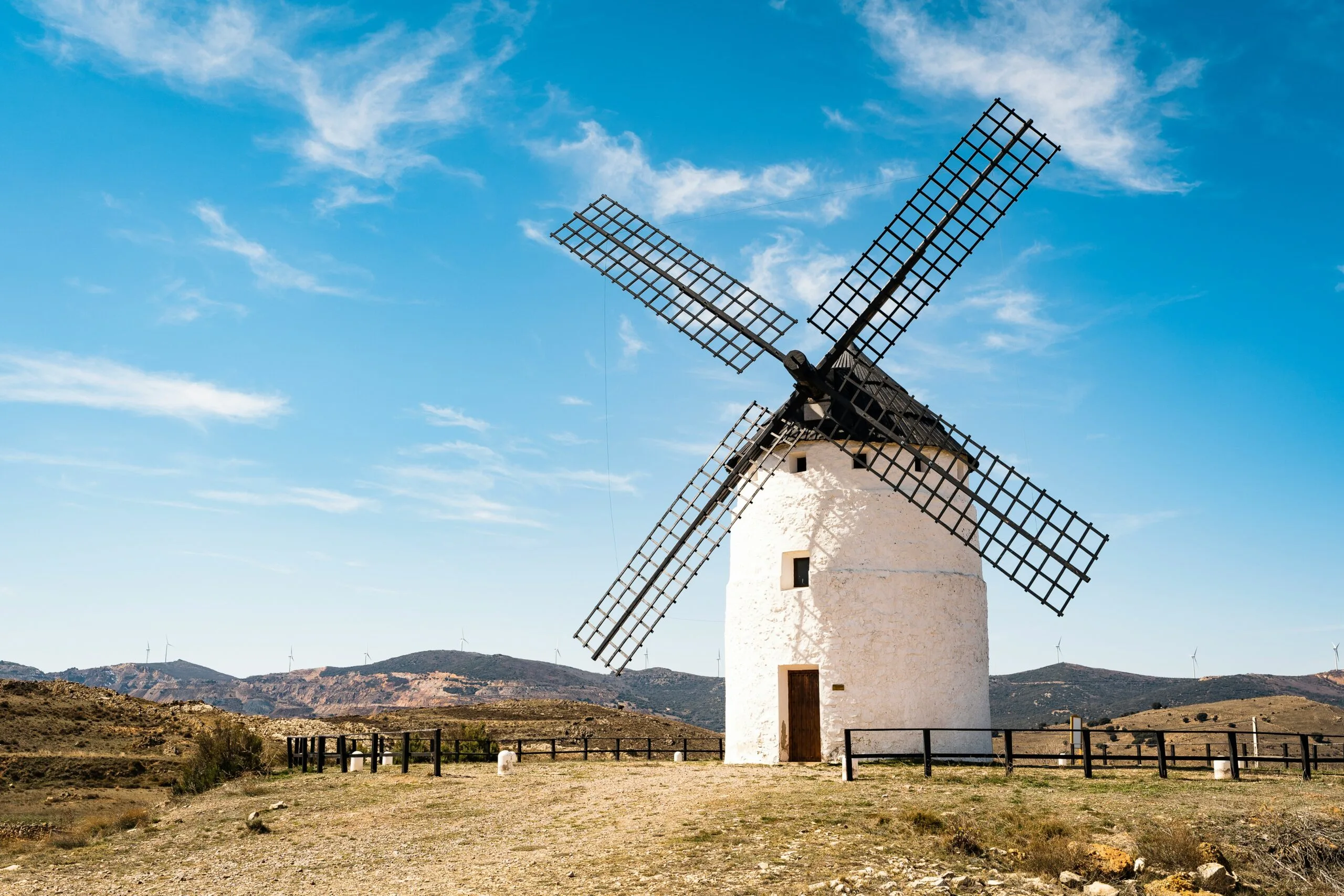 A white windmill with black blades on a hill under a blue sky.