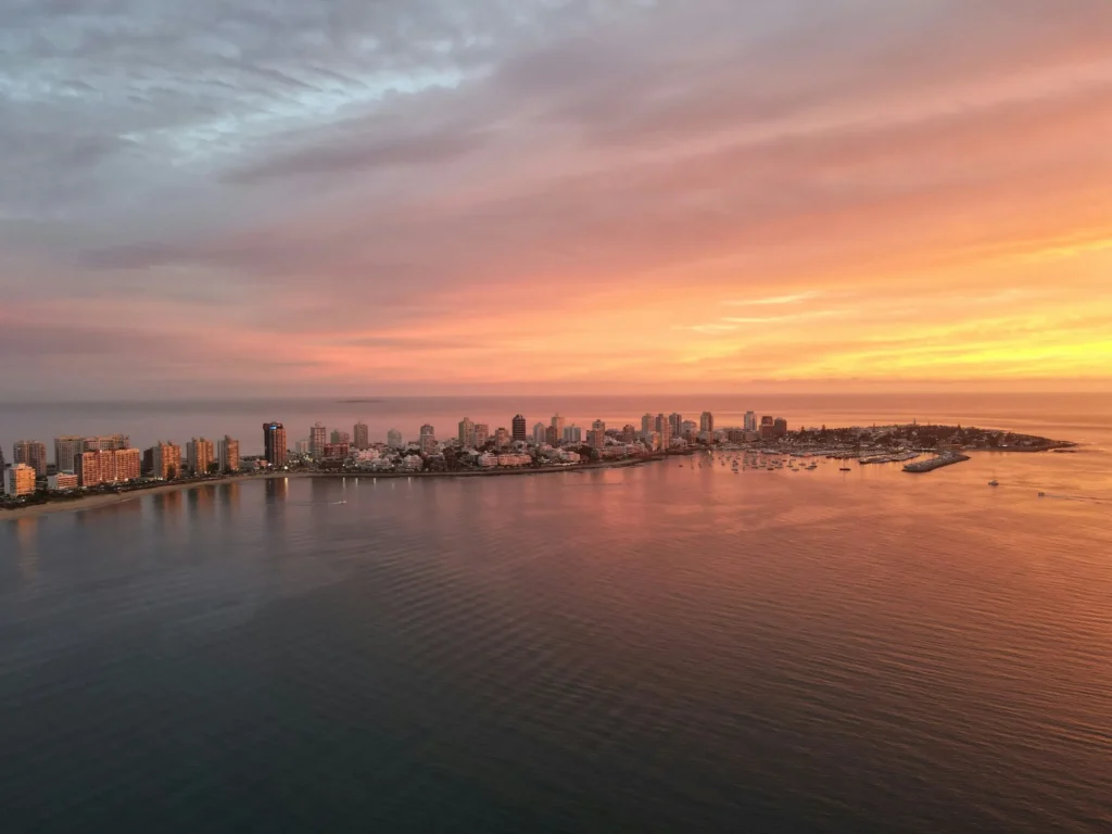 A panoramic view of a Punta del Este at sunset, with a vibrant orange and pink sky.