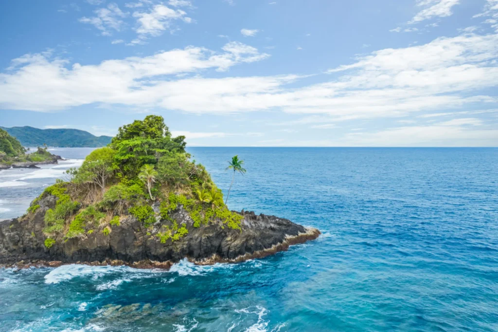 A small, rocky island covered in green vegetation rises from the clear blue ocean.