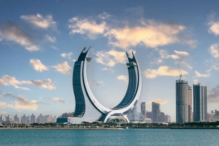 A modern, circular-shaped building standing prominently on a waterfront with a city skyline in the background.