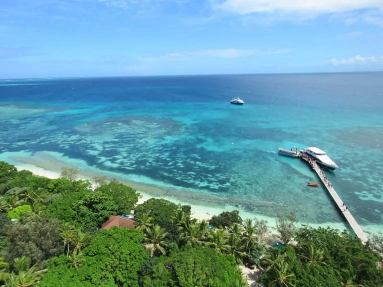 An aerial view of a tropical coastline with clear turquoise water, coral reefs, and lush green islands.
