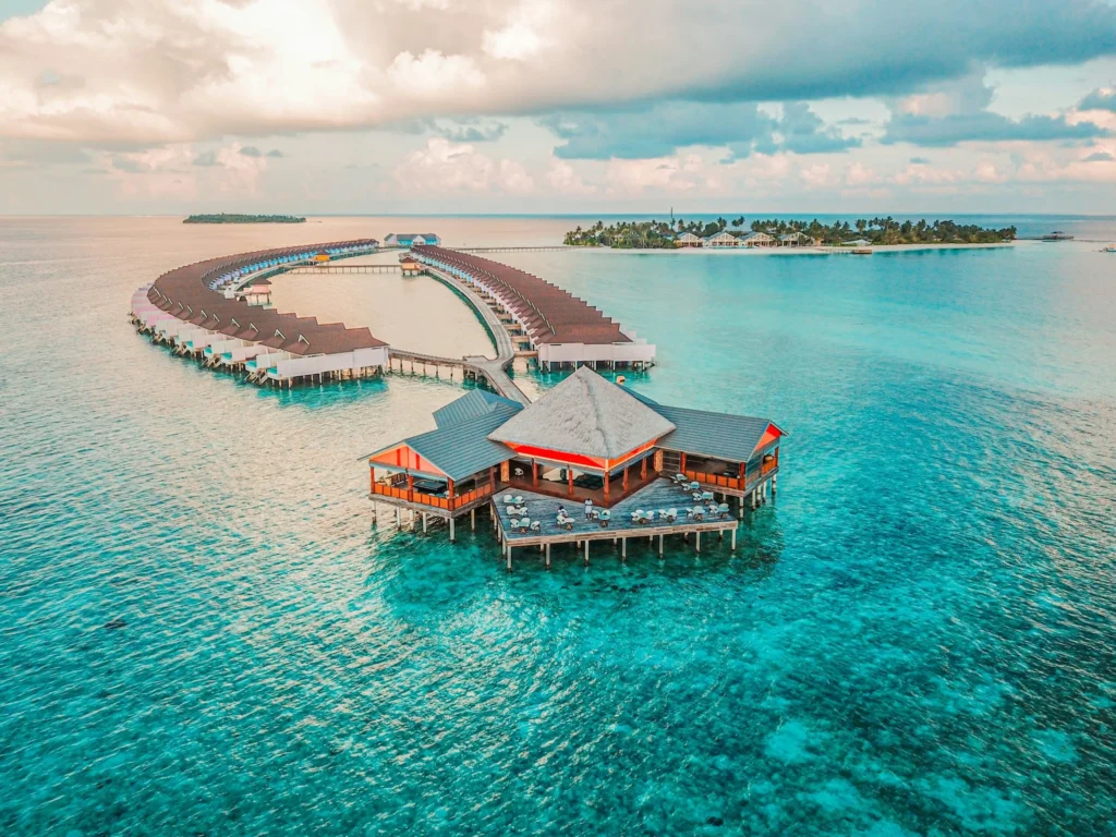 An aerial view of luxurious overwater bungalows and resorts arranged in a circular pattern over crystal-clear turquoise water.