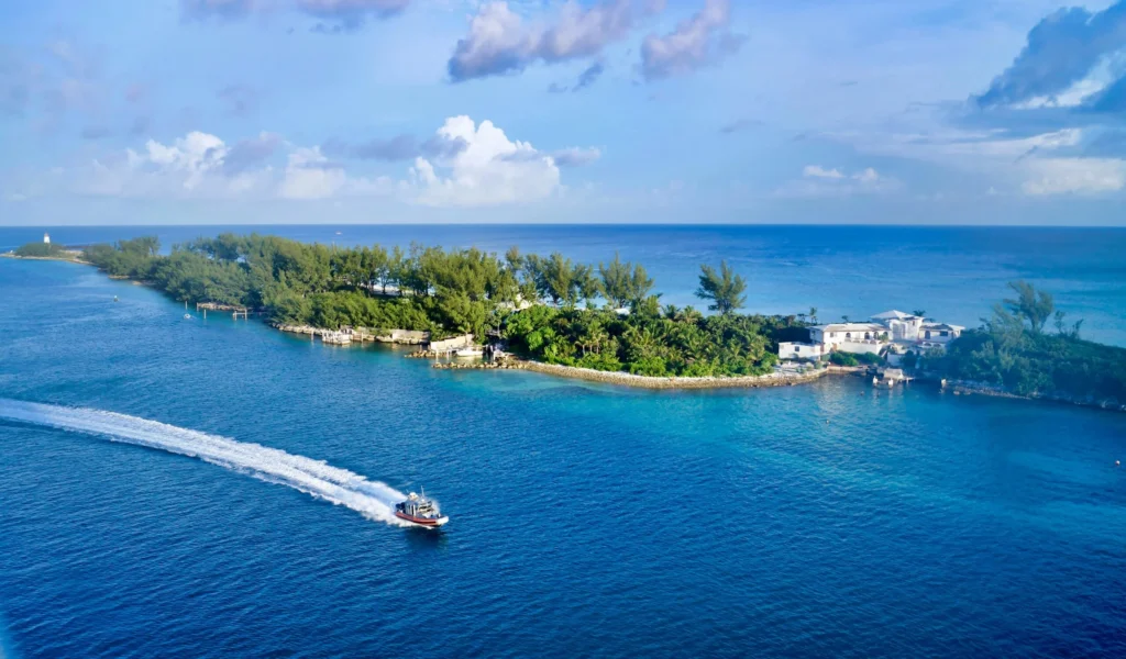 An aerial view of a small island with lush vegetation surrounded by clear blue water, with a boat leaving a wake.