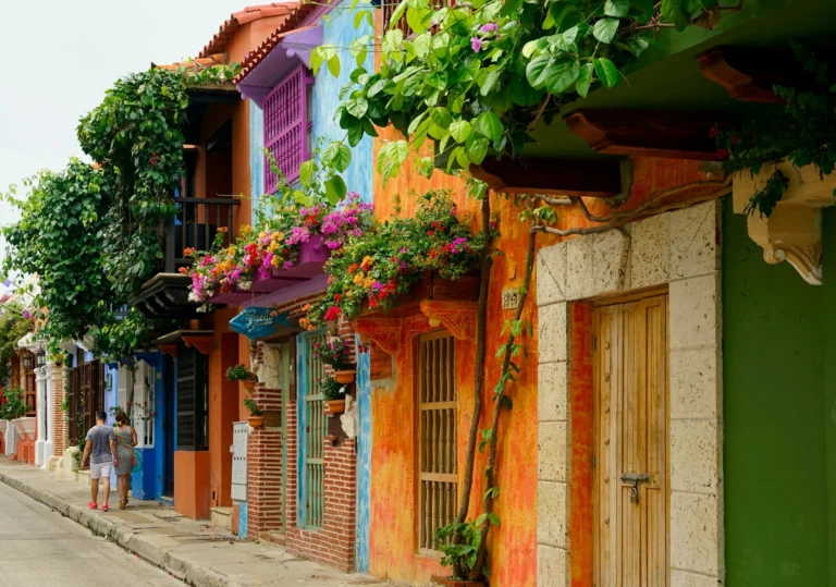 A colorful street scene with brightly painted buildings and flowers on balconies.
