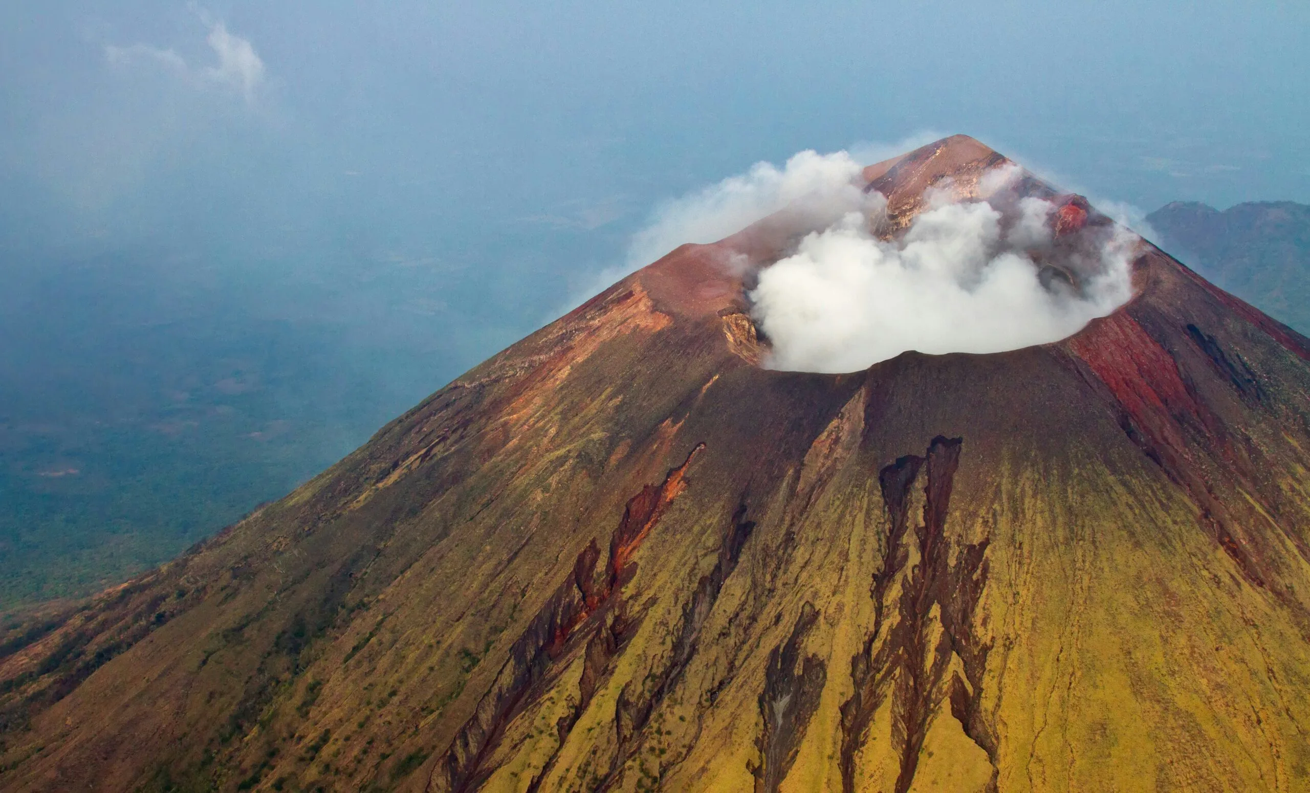 An aerial view of a volcano with smoke emanating from its crater.
