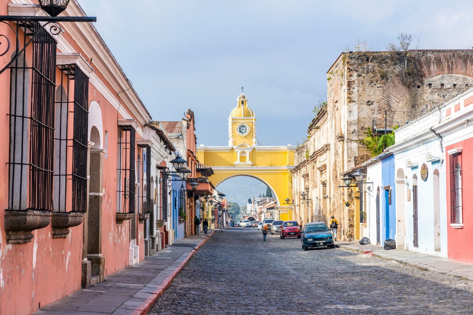 A cobblestone street in a colonial town with colorful buildings and an archway.