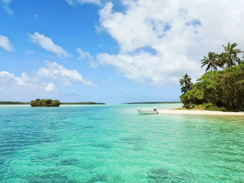 A small, sandy island with palm trees in clear turquoise water, with a boat nearby.
