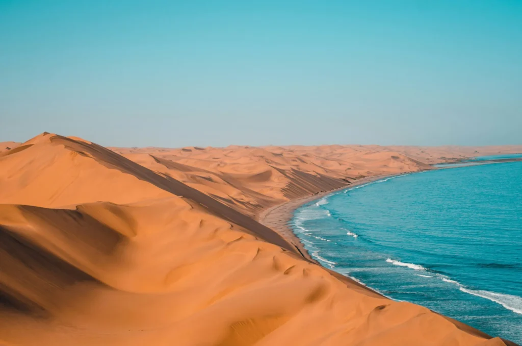 A vast desert landscape with red sand dunes meeting the turquoise ocean.
