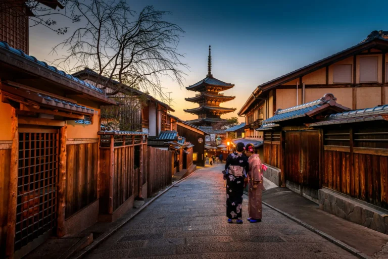 A traditional Japanese street scene with wooden buildings, a pagoda, and two people walking away.