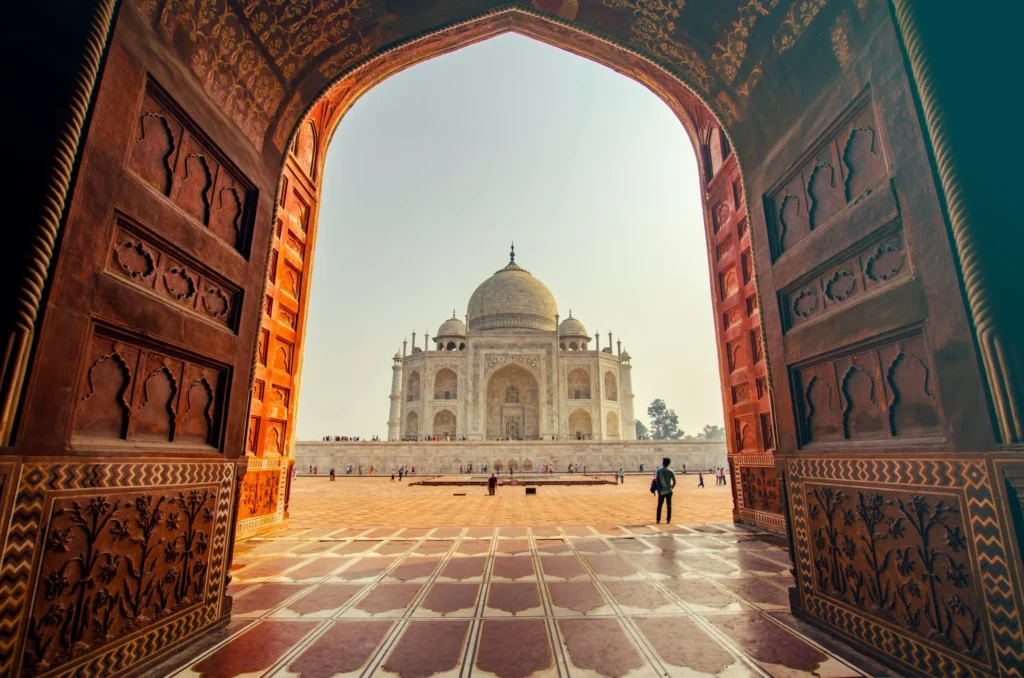 A view of the Taj Mahal through an arched doorway, with a person standing in the foreground.