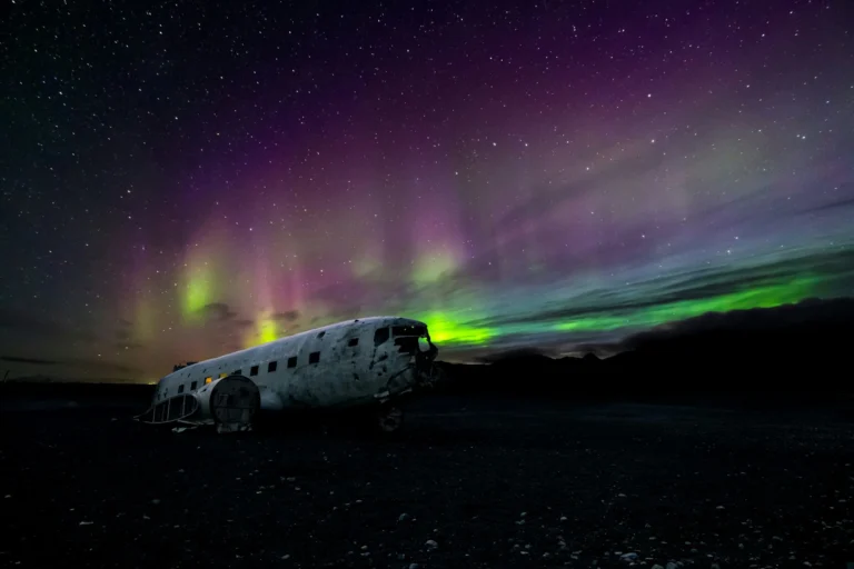 The Northern Lights illuminating the sky above a wrecked airplane fuselage on a dark landscape.