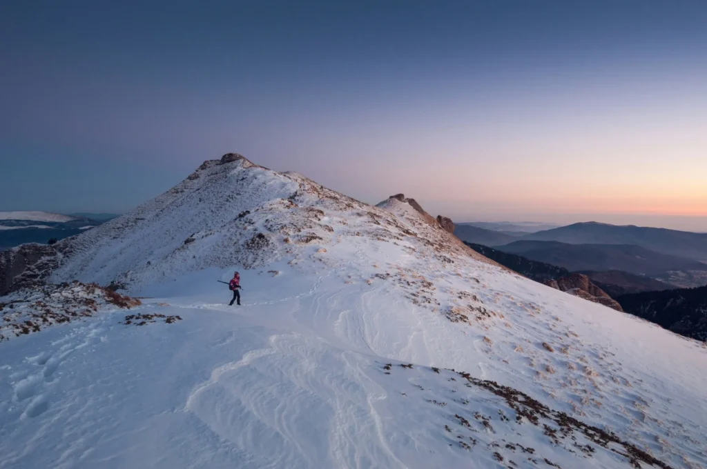 A snow-covered mountain peak against a dramatic sunset or sunrise sky.