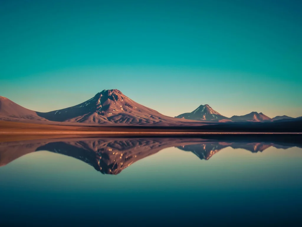 A serene desert landscape with a still body of water reflecting the mountains under a gradient sky.